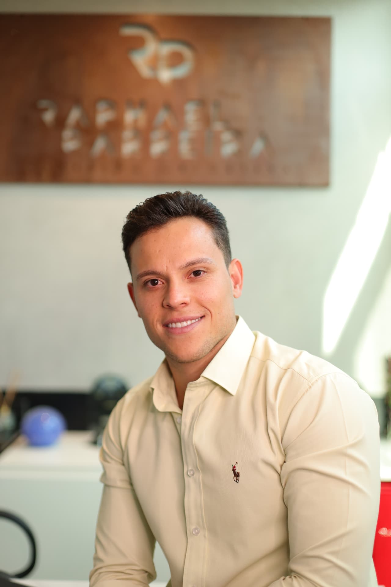 Raphael Parreira sorrindo em seu escritório de consórcios, pronto para atender clientes de imóvel, carro e moto